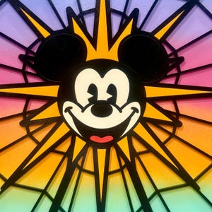 Puede incluir: Una imagen colorida de estilo vitral de Mickey Mouse con un estallido de estrella amarilla detr&aacute;s de &eacute;l. El fondo es un degradado de morado, rosa, naranja, amarillo, verde y azul.