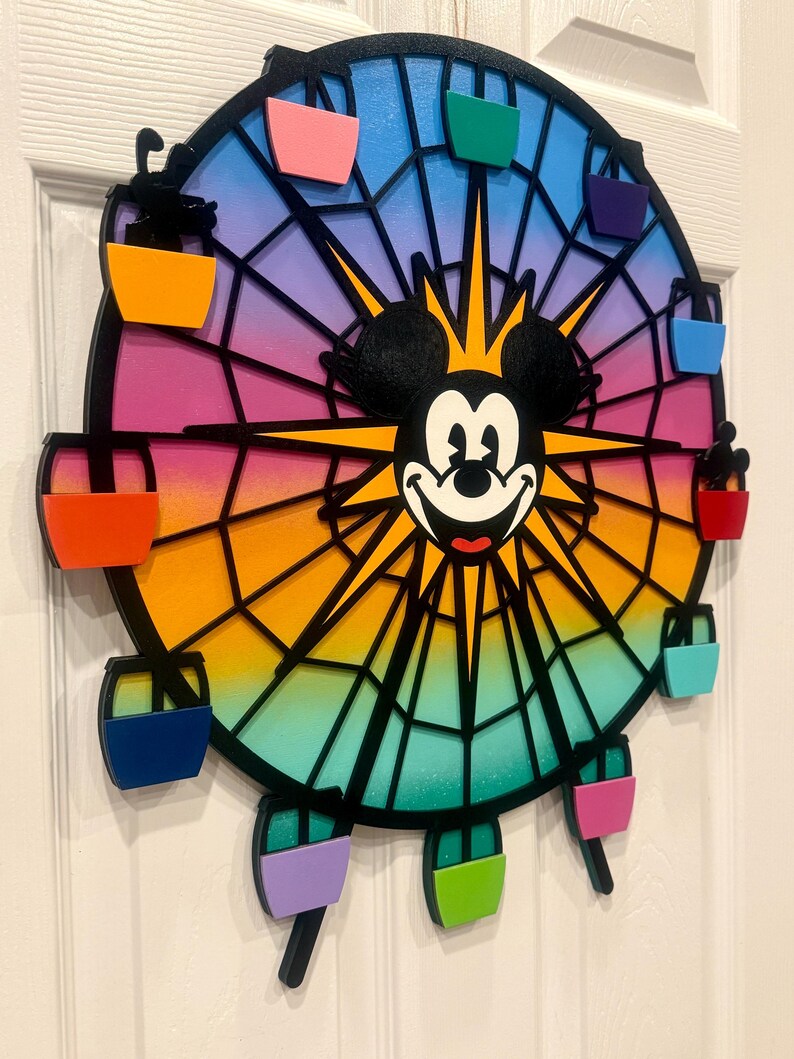 Puede incluir: Una noria de madera colorida con Mickey Mouse en el centro. La noria tiene ocho g&oacute;ndolas, cada una pintada de un color diferente: rojo, naranja, amarillo, verde, azul, morado, rosa y negro.