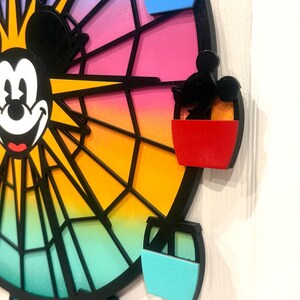 Puede incluir: Una ilustraci&oacute;n en blanco y negro de Mickey Mouse en una noria colorida con g&oacute;ndolas rojas, azules y amarillas. La noria est&aacute; pintada con un degradado de rosa, naranja, amarillo, verde y azul.