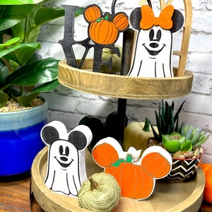 May include: A tiered wooden tray with Halloween decorations. The top tier has a black wooden "LOVE" sign with a pumpkin-shaped Mickey Mouse head. The bottom tier has a white ghost with Mickey Mouse ears, a pumpkin-shaped Mickey Mouse head, and a gold pumpkin.