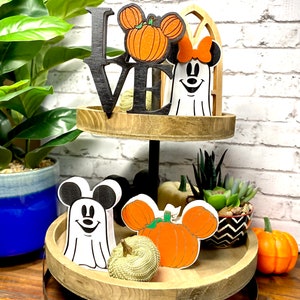 May include: A two-tier wooden tray with a black "LOVE" sign, a white ghost with a red bow, a pumpkin with Mickey Mouse ears, and a white ghost with Mickey Mouse ears. The tray is decorated with pumpkins, succulents, and a black and white patterned bowl.