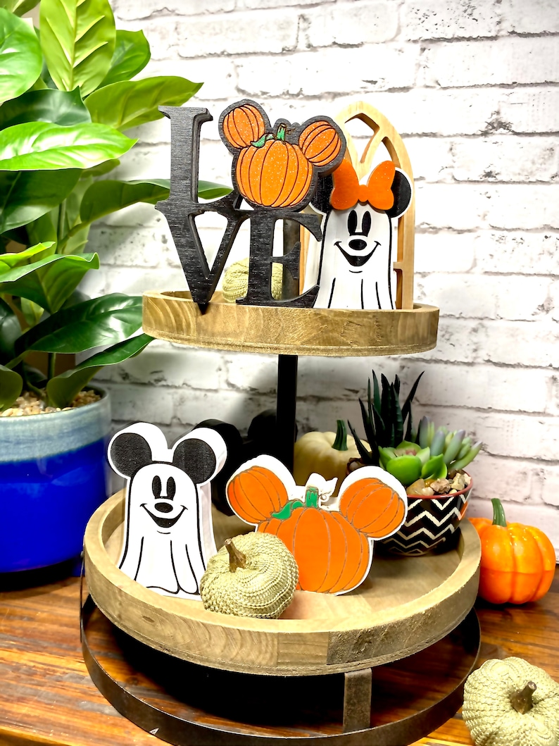 May include: A two-tier wooden tray with a black "LOVE" sign, a white ghost with a red bow, a pumpkin with Mickey Mouse ears, and a white ghost with Mickey Mouse ears. The tray is decorated with pumpkins, succulents, and a black and white patterned bowl.