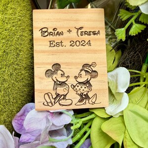May include: A rectangular light-colored wooden plaque featuring a laser-engraved design of two cartoon mice facing each other. The text "Brian + Teresa" is engraved above the phrase "Est. 2024" in a dark, clear font centered on the wood grain surface.