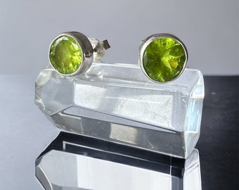 May include: A pair of silver stud earrings with round green peridot gemstones.