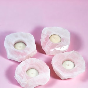 Könnte beinhalten: Vier rosa Kristall-Kerzenhalter mit einer glatten, polierten Oberfläche. Jeder Halter hat eine runde, vertiefte Fläche für ein Teelicht.