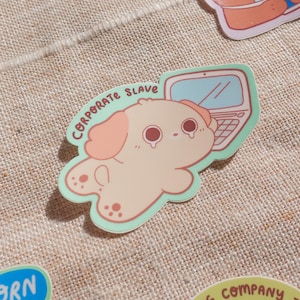 May include: A sticker depicting a cartoon dog and a laptop, with the dog appearing to cry. The dog is light peach with pink ears and spots, and the laptop is light blue. The text "CORPORATE SLAVE" is above the dog. The sticker has a light green border.