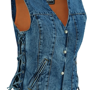 Könnte beinhalten: Eine blaue Jeansweste mit Schnürung an der Seite, Reißverschlusstaschen und Knopfverschluss. Die Weste hat ein braunes Netzfutter und ein Etikett mit der Aufschrift "ANCE Leather Co."