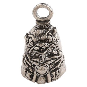 Op de afbeelding: Zilverkleurige motorbel met een gedetailleerd, gebeeldhouwd ontwerp van een grotesk gezicht. De bel heeft een lus aan de bovenkant om op te hangen en een uitlopende bodem. Het gezicht heeft overdreven kenmerken en is het middelpunt van het ontwerp van de bel.