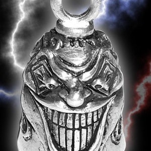 May include: A silver motorcycle handlebar bell with a detailed design of a grinning, evil clown face.