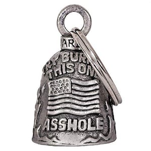 Op de afbeelding: Een zilverkleurige bel met een ring om op te hangen. De bel heeft een Amerikaans vlagontwerp en de woorden "Ride 'em Burn This On Asshole". De bel is waarschijnlijk voor een motorfiets of een vergelijkbaar voertuig.