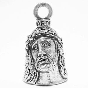 Op de afbeelding: Een zilverkleurige bel met een gedetailleerde afbeelding van een persoon met een doornenkroon. Het woord "ARDI" is zichtbaar op de bovenkant van de bel. De bel heeft een lus om op te hangen.