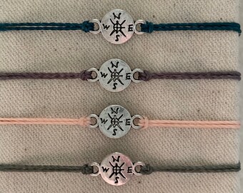 May include: Four bracelets with compass charms. The bracelets are teal, grey, pink, and green.