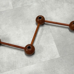 May include: A wooden candle holder with a unique design. It features four spherical candle holders connected by straight wooden rods. The candle holders and rods are a warm brown color, creating a natural aesthetic.