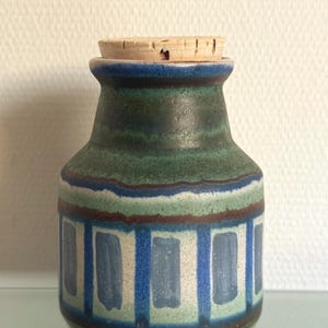 Op de afbeelding: Een kleine keramische pot met een kurken stop, voorzien van een cilindrisch lichaam en een taps toelopende hals. Het oppervlak is versierd met horizontale banden in donkerblauw, bosgroen en crème, geaccentueerd door een patroon van verticale blauwe rechthoeken.