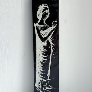 Może przedstawiać: Czarny, prostokątny obraz na ścianę z białą ilustracją kobiety trzymającej dziecko. Grafika ma minimalistyczny design, z postaciami przedstawionymi w prostych liniach i kształtach. Obraz ma błyszczące wykończenie.