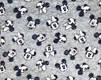 Op de afbeelding: Een grijze stof met een herhalend patroon van zwarte en witte Mickey Mouse en Minnie Mouse gezichten.