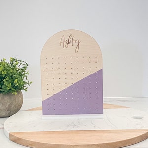 Arch-shaped earring stand engraved with a girl's name and stands on a display block. Lavender is painted across the earring stand that can be customized with your favorite color.
