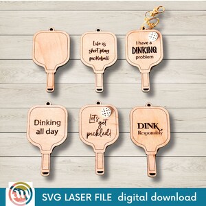 Könnte beinhalten: Sechs Holz-Pickleball-Schläger-Ornamente mit verschiedenen Sprüchen. Die Sprüche lauten "Life is short play pickleball", "I have a dinking problem", "Dinking all day", "Let's get pickled!", "DINK Responsibly" und ein leerer Schläger.