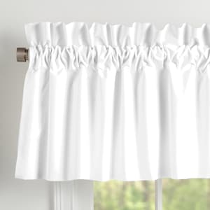 May include: A white, gathered valance curtain. The fabric is a solid white color, with a ruffled top edge. The curtain is hanging on a silver-colored rod, and the bottom edge is straight. The curtain is hanging in front of a window.