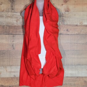 May include: A red sleeveless cardigan with a draped, asymmetrical design. The cardigan is made of a soft, lightweight fabric and has a relaxed fit.