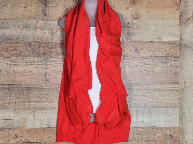 May include: A red sleeveless cardigan with a draped, asymmetrical design. The cardigan is made of a soft, lightweight fabric and has a relaxed fit.