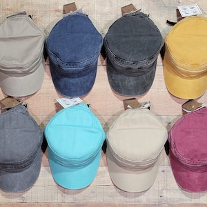 May include: Eight different colored cotton twill baseball caps with a flat brim and a single button on top. The caps are hanging on a wooden wall.
