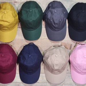 May include: Eight blank baseball caps in different colors: yellow, green, gray, black, maroon, navy blue, beige, and pink. The caps are arranged in two rows of four, with the brim facing the viewer.