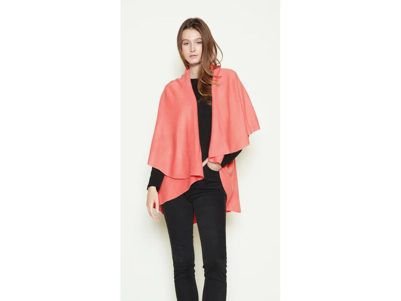 May include: A coral pink wrap with a draped design. The wrap is made of a soft, lightweight fabric and is perfect for layering over a simple outfit.