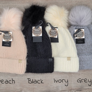 May include: Four faux fur pom pom beanies in peach, black, ivory, and gray. Each beanie has a tag that reads "Cruelty-Free Fashion Vegan Faux Fur David and Young".