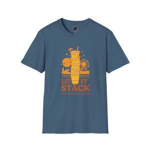 May include: A blue t-shirt with a graphic design featuring a stack of yellow cups with a straw and umbrella, a Ferris wheel, and the text "LET IT STACK YELLOW CUP CLUB".