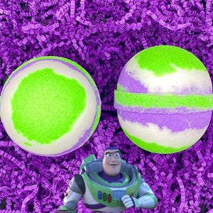 May include: Two green, white, and purple bath bombs with a space ranger character in the foreground.