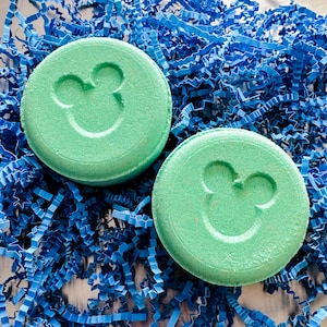 Op de afbeelding: Twee groene badbommen met een Mickey Mouse silhouetontwerp. De badbommen liggen op een blauwe, gescheurde papieren achtergrond.