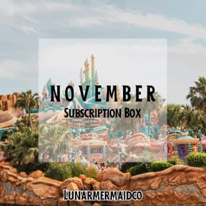 May include: A subscription box promotional graphic featuring a fantasy-themed castle with teal spires and rock formations. The text NOVEMBER SUBSCRIPTION BOX is centered, and LUNARMERMAIDCO is printed at the bottom against a sky background.