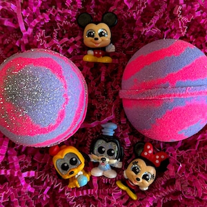 Peut inclure: Deux bombes de bain violettes et roses avec des paillettes, entourées de cinq petites figurines de personnages Disney. Les figurines sont Mickey Mouse, Minnie Mouse, Pluto, Dingo et Donald Duck.