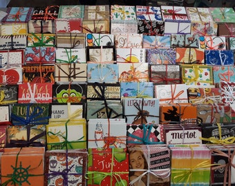 May include: A collection of small, square, colorful coasters with various designs and text. The coasters are stacked and tied with ribbon. Some of the designs include a baseball, a lobster, a firefighter, a llama, a dog, a witch, a skull, and a wine glass. The text on the coasters includes "Let's Pawty!" and "Merlot".