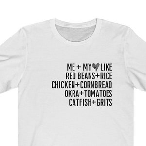 May include: White t-shirt with black text that reads "ME + MY LIKE RED BEANS+RICE CHICKEN CORNBREAD OKRA+TOMATOES CATFISH+GRITS"