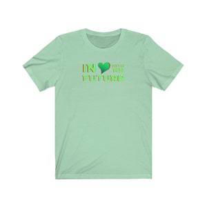 Op de afbeelding: Een lichtgroen T-shirt met een grafisch ontwerp dat "IN &hearts; WITH MY FUTURE" zegt in een regenboogkleurenschema.