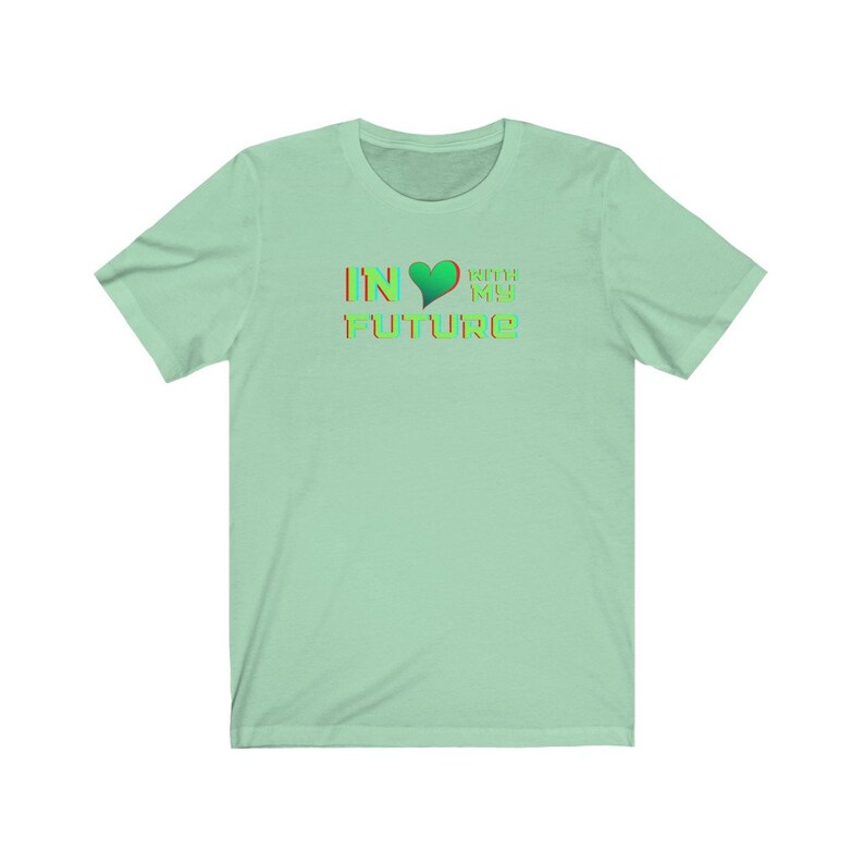 Op de afbeelding: Een lichtgroen T-shirt met een grafisch ontwerp dat "IN &hearts; WITH MY FUTURE" zegt in een regenboogkleurenschema.