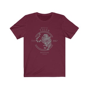 Könnte beinhalten: Ein maroonfarbenes T-Shirt mit einer grauen Grafik eines Tigers in einem Kreis. Der Kreis enthält den Text "HOUSE TIGER EST. 1947 HOUSTON TEXAS".