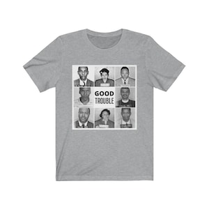Könnte beinhalten: Ein graues T-Shirt mit einem Schwarzweißbild von acht Personen in Polizeifotos. Der Text "GOOD TROUBLE" ist unter dem Bild gedruckt.