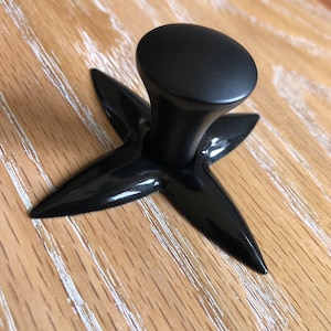 May include: Black cabinet knob with a four-pointed star base.