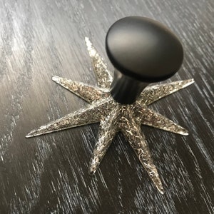 May include: A black star-shaped knob with a silver glitter finish. The knob has a round, black top.