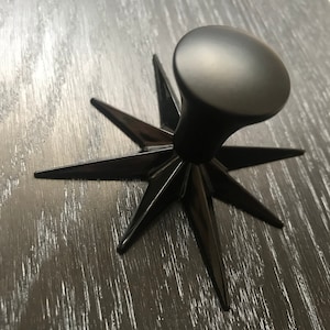 May include: Black cabinet knob with a star-shaped base and a round top.