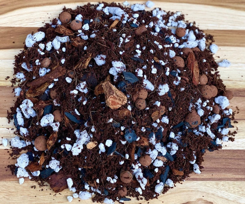 May include: A close-up of a brown potting mix with white perlite, black charcoal, and brown bark pieces. The mix is ideal for growing plants.