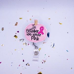 May include: Pink glitter pumpkin-shaped badge holder with a pink ribbon and the text "In October we wear pink".