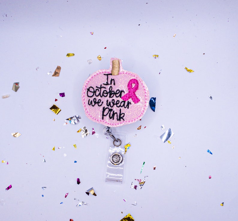 May include: Pink glitter pumpkin-shaped badge holder with a pink ribbon and the text "In October we wear pink".