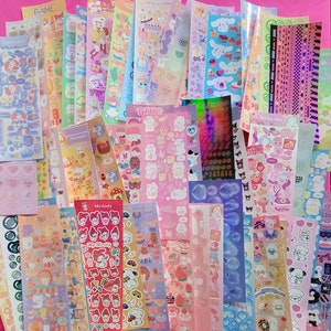 May include: A collection of colorful sticker sheets featuring various cute cartoon characters, including animals, food, and other whimsical designs. The stickers are perfect for decorating planners, journals, laptops, and other personal items.