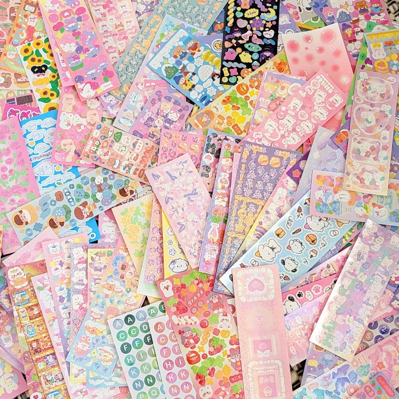 May include: A collection of colorful, patterned, and glittery stickers featuring various designs, including animals, flowers, and geometric shapes. The stickers are arranged in a random pattern on a white surface.
