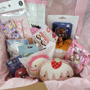 May include: A pink and white gift box filled with various items, including a pink and white cake-shaped coin purse, a pink and white character keychain, a pink and white character plush toy, a blue and white character plush toy, a blue and white character pouch, a pink and white character pouch, a pink and white character sticker sheet, a blue and white character sticker sheet, a pink and white character card, a blue and white character card, a pink and white character bag, a blue and white character bag, and a pink and white character bag.