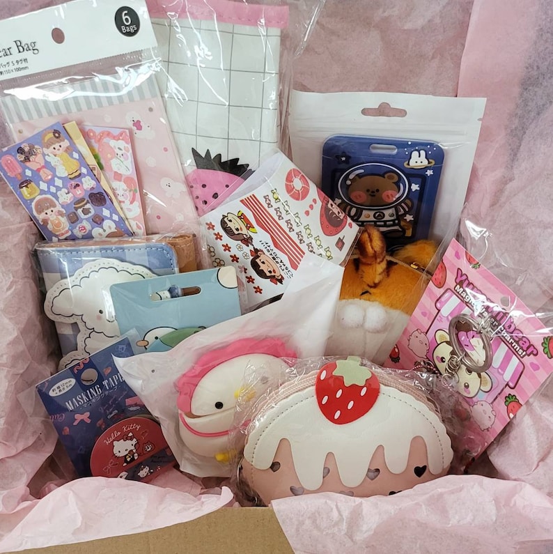 May include: A pink and white gift box filled with various items, including a pink and white cake-shaped coin purse, a pink and white character keychain, a pink and white character plush toy, a blue and white character plush toy, a blue and white character pouch, a pink and white character pouch, a pink and white character sticker sheet, a blue and white character sticker sheet, a pink and white character card, a blue and white character card, a pink and white character bag, a blue and white character bag, and a pink and white character bag.